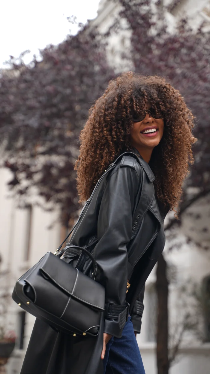 Mujer con trench negro sonriendo, bolso de cuero negro