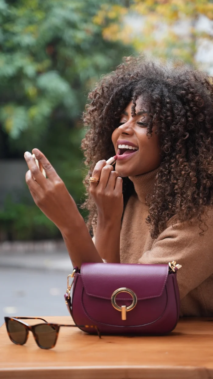 Mujer sonriendo con bolso de cuero burdeo y lentes de sol